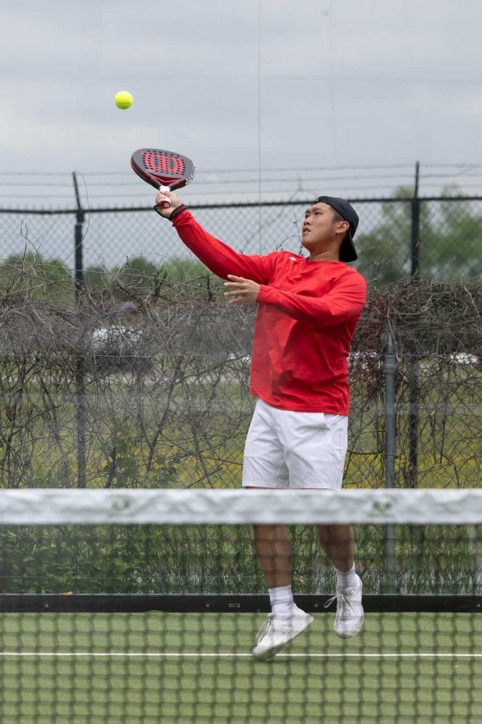 Padel player reaching for a high ball during a rally at Glassbox Padel Club