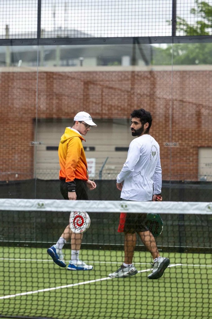Two padel players chatting across the net during a friendly match at Glassbox